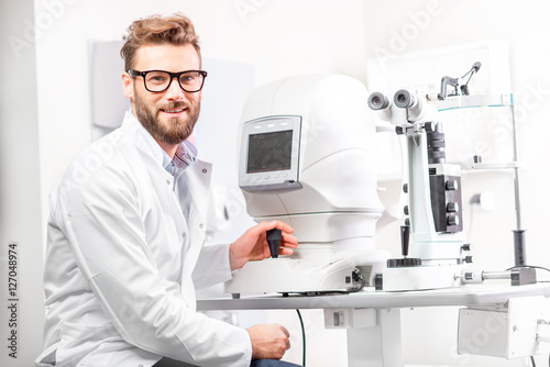 Portrait of handsome eye doctor sitting with ophthalmologic device in the cabinet