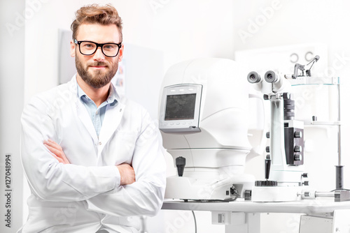Portrait of handsome eye doctor sitting with ophthalmologic device in the cabinet