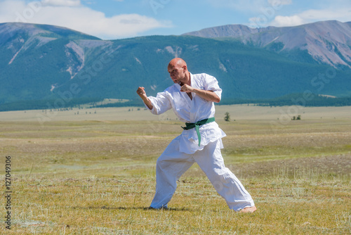 Man in white kimono and black belt training kung-fu, karate or aikido on mountain background.
