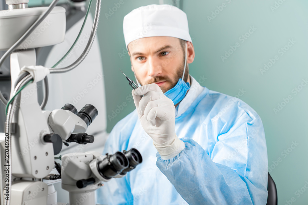 Eye surgeon holding small surgical scissors for eye operation in the operating room near the microscope. Image with small deph of field focused on hands and scissors Eye surgeon holding small surgical scissors for eye operation in the operating room near the microscope. Image with small deph of field focused on hands and scissors