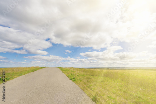 Asphalt road through the field with green grass under blue sky with clouds