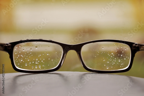 Glasses in a black frame with raindrops on the lens close-up. Blurred autumn background.