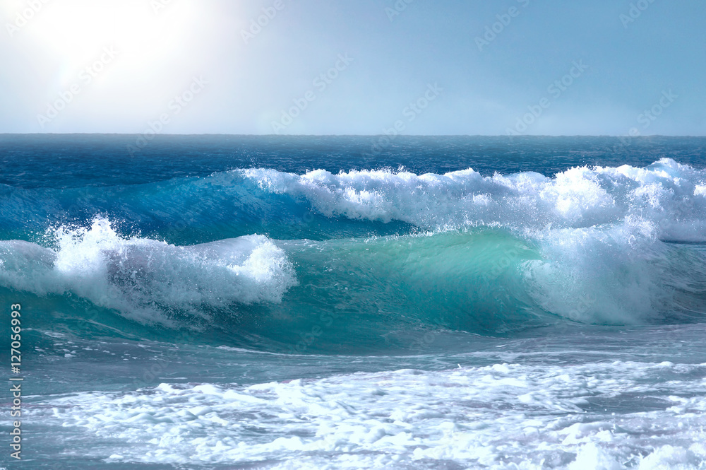 Beautiful big waves of the ocean or the sea in the summer bright blue, azure and turquoise colors in the early morning in sun light on a pure blue sky. Beautiful combs white sea foam.