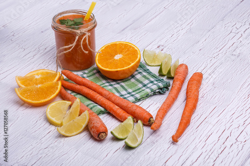 orange detox coctail with oranges and carrots lies on white tabl