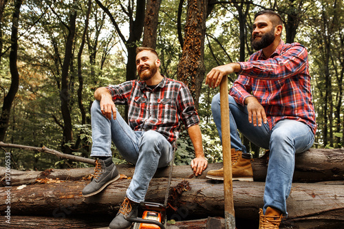Two friends Lumberjack worker sitting in the forest .Resting after hard work.