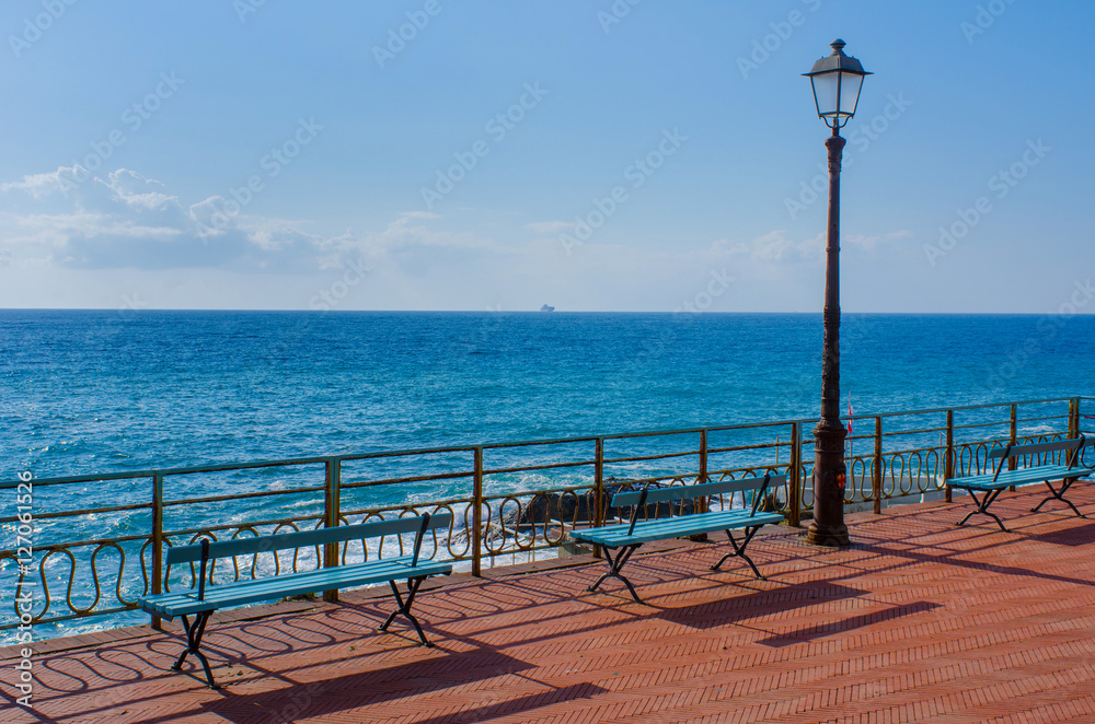 two benches and an old lantern on the walking promenade of Nervi, Genoa, in Italy with a wonderful view to the Mediterranean Sea on a sunny day with a boat visible far away on the horizon