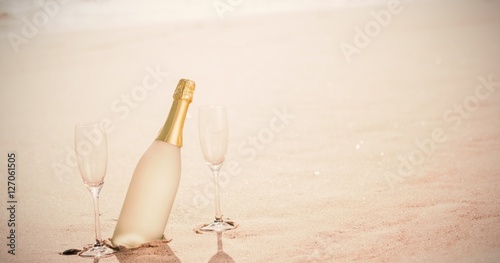 Champagne flutes with bottle on sand at beach photo