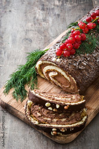 Foto Chocolate yule log christmas cake with red currant on wooden background