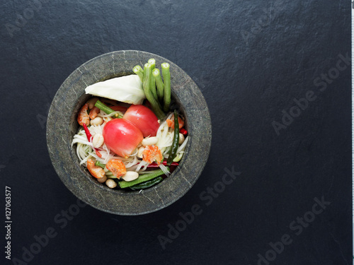 Thai green papaya salad (Som tum) in granite mortar on dark background