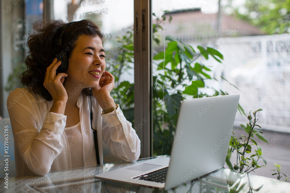Asian girl enjoying music in headphones sitting with a laptop in a cafe. Asian girl enjoying music in headphones sitting with a laptop in a cafe.