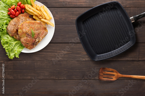 Top view pork chop steak, grill pan and spatula on the wooden background.