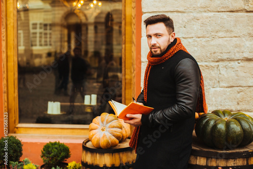 handsome and young man in a black coat reading a book outdoors photo