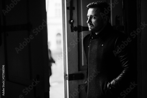 handsome and young man in a black coat standing near doors photo