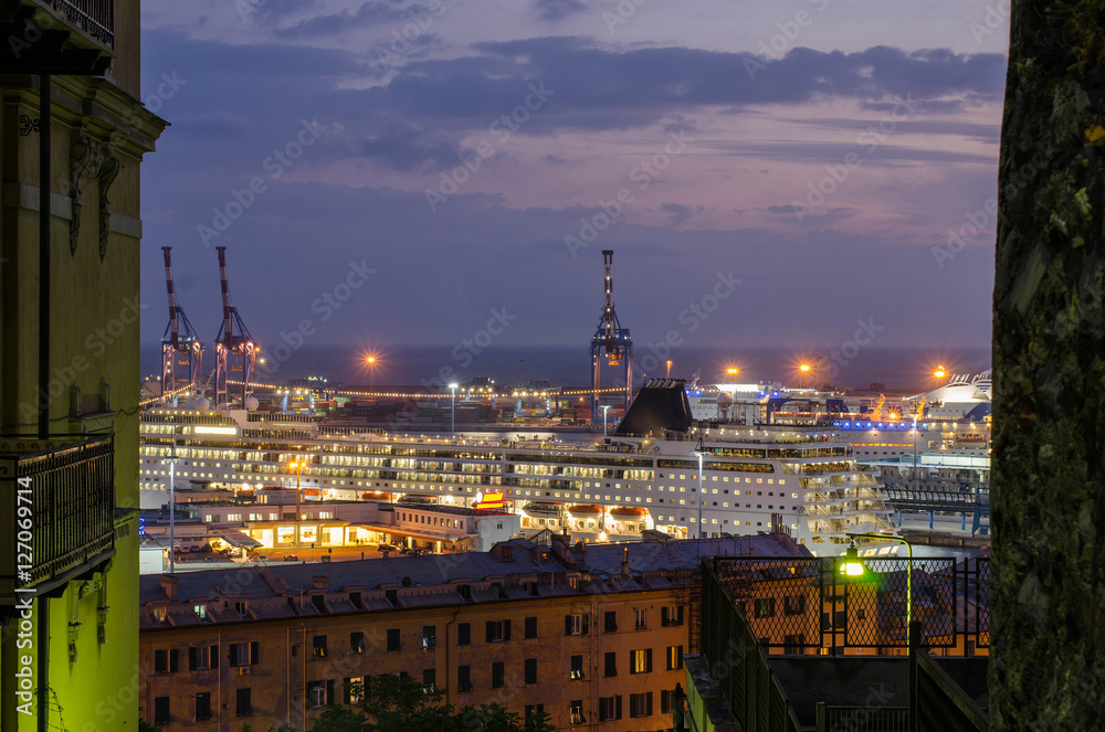 View of the Genoa harbor with ships and container cranes from the inside of the city in the beautiful lit up evening.