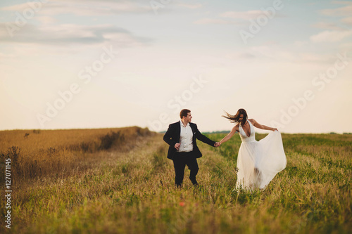 happy and young bride and groom running in the field