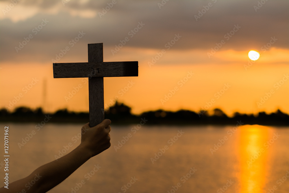 Close up woman hand holding wood cross or religion symbol shape over a sunset sky with clouds background for God,Christianity, religious, 
