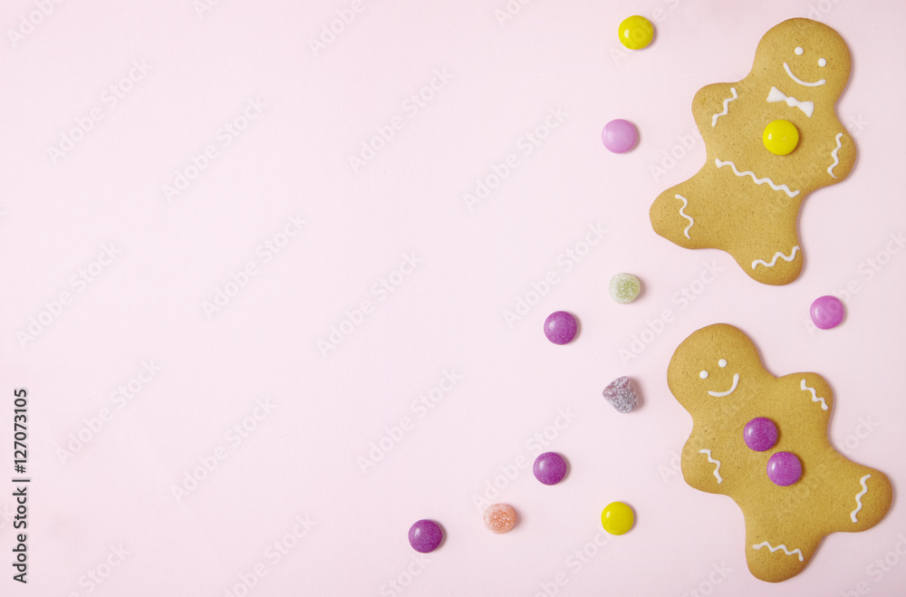 Obraz premium Hand decorated gingerbread men on a pastel pink background, with sweets and blank space at side