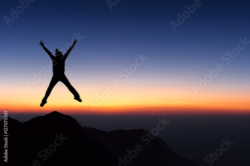 Woman on top of mountain jumping and looking to sunset sky.