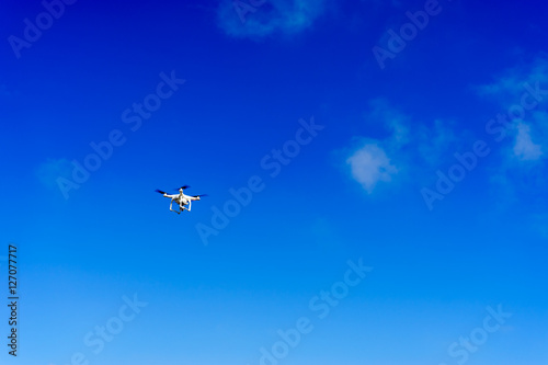 white drone with video camera in bright blue sky. white drone under blue sky.
