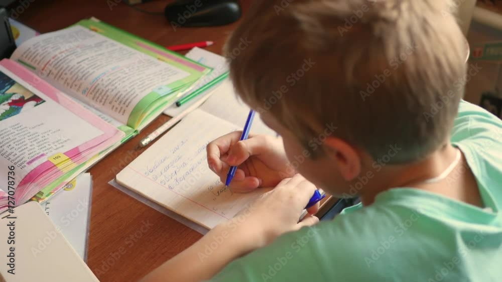 the child does his homework, writes in a copybook at table the child does his homework, writes in a copybook at table