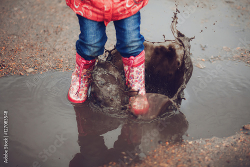 Child wearing pink rain boots jumping into a puddle