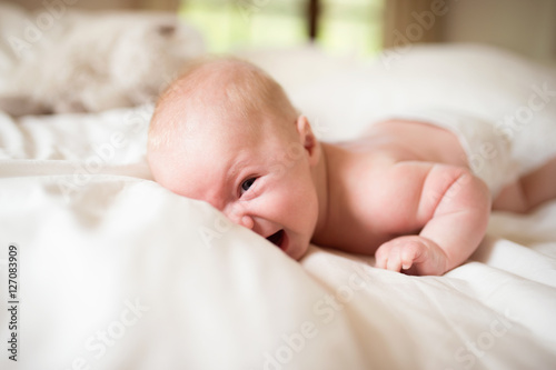 Little baby boy lying on bed making funny face, laughing.