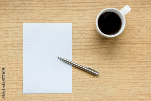 Workplace of wooden desk with a pen and empty white paper with a cup of coffee