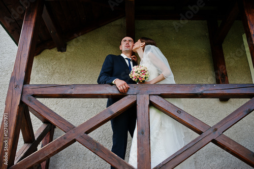 Wedding couple stay on the balcony near the wooden railing. Brid