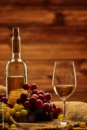 Fototapeta Naklejka Na Ścianę i Meble -  Bottle of white wine, glass and grape on a sack in wooden interi
