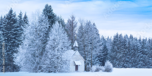 Christmas serene winter panoramic landscape with tiny woody chapel in snowy frozen forest photo