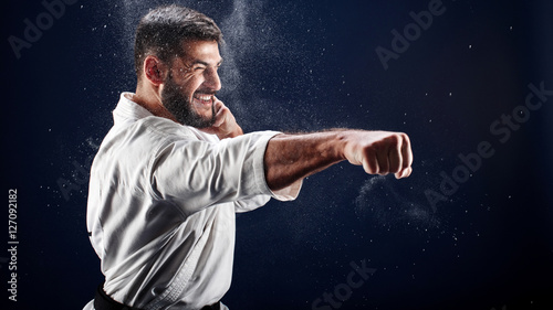 Karate man in a kimono hits a hand on blue background photo