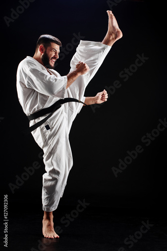 Karate man in a kimono hits foot on a black background