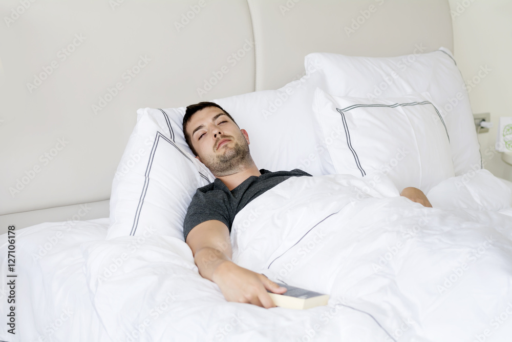 Handsome young man happily sleeping in white bed with book in the hand Handsome young man happily sleeping in white bed with book in the hand