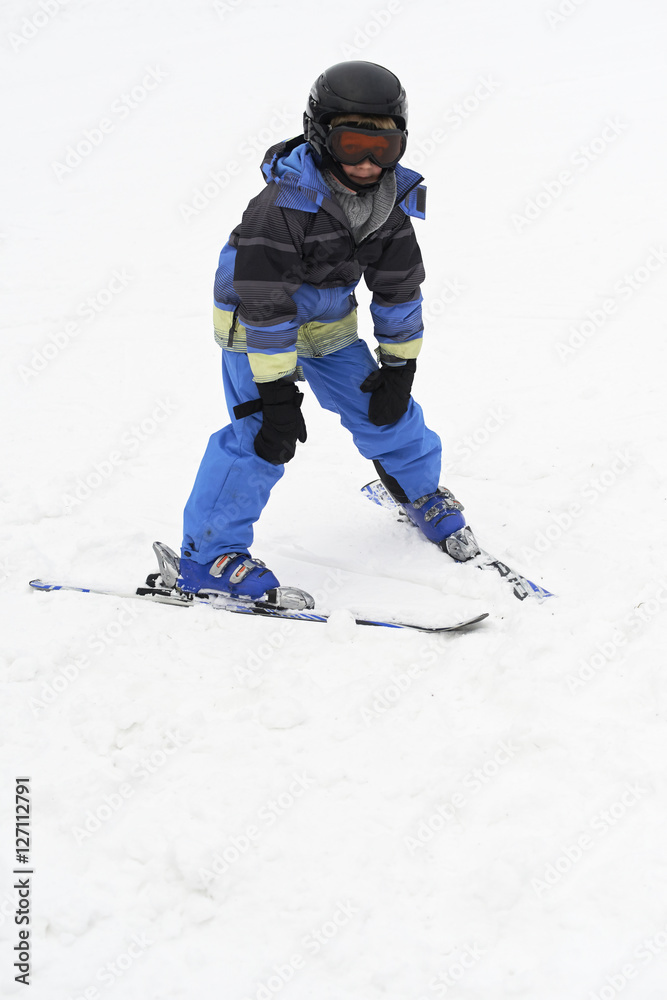 Child boy skiing in mountains. Active teenager kid with safety helmet and goggles. Ski race for