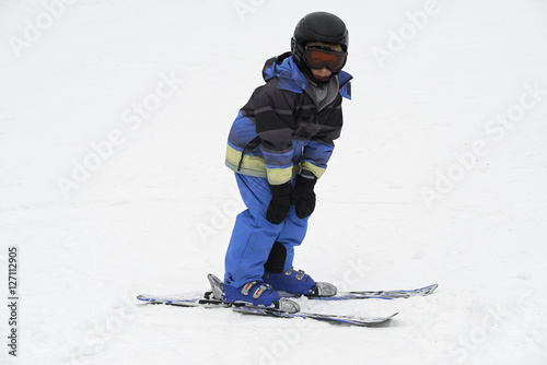 Child boy skiing in mountains. Active teenager kid with safety helmet and goggles. Ski race for young children. Winter sport for family. Kids ski lesson in alpine school. Young skier racing in snow