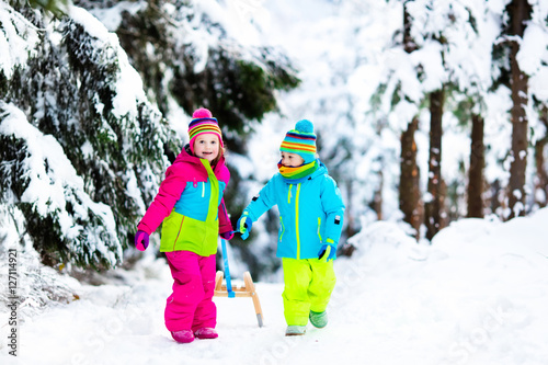 Children play in snow on sleigh in winter park