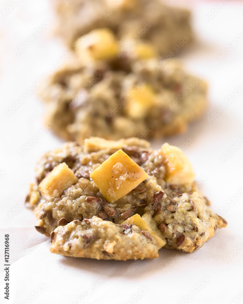 Freshly baked apple, oatmeal and linseed cookies on baking paper, photographed with natural light (Selective Focus, Focus in the middle of the first cookie) Freshly baked apple, oatmeal and linseed cookies on baking paper, photographed with natural light (Selective Focus, Focus in the middle of the first cookie)