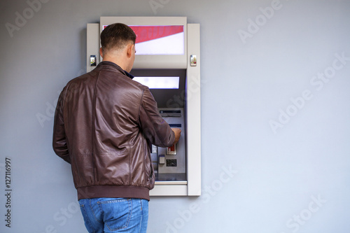 Young man inserting a credit card to ATM