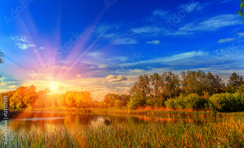 Colorful majestic sunset with a ãàëî and of sunlight. picturesque scene. breathtaking scenery. Colorful summer sunrise over lake in forest. fantastic view. use as background. original creative images