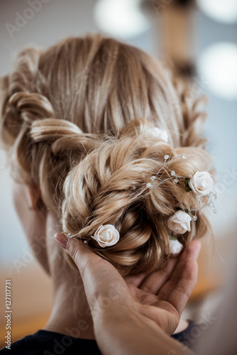 Female hairdresser making hairstyle to blonde girl in beauty salon.