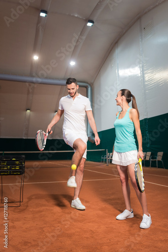 Professional delighted instructor teaching young woman to play tennis