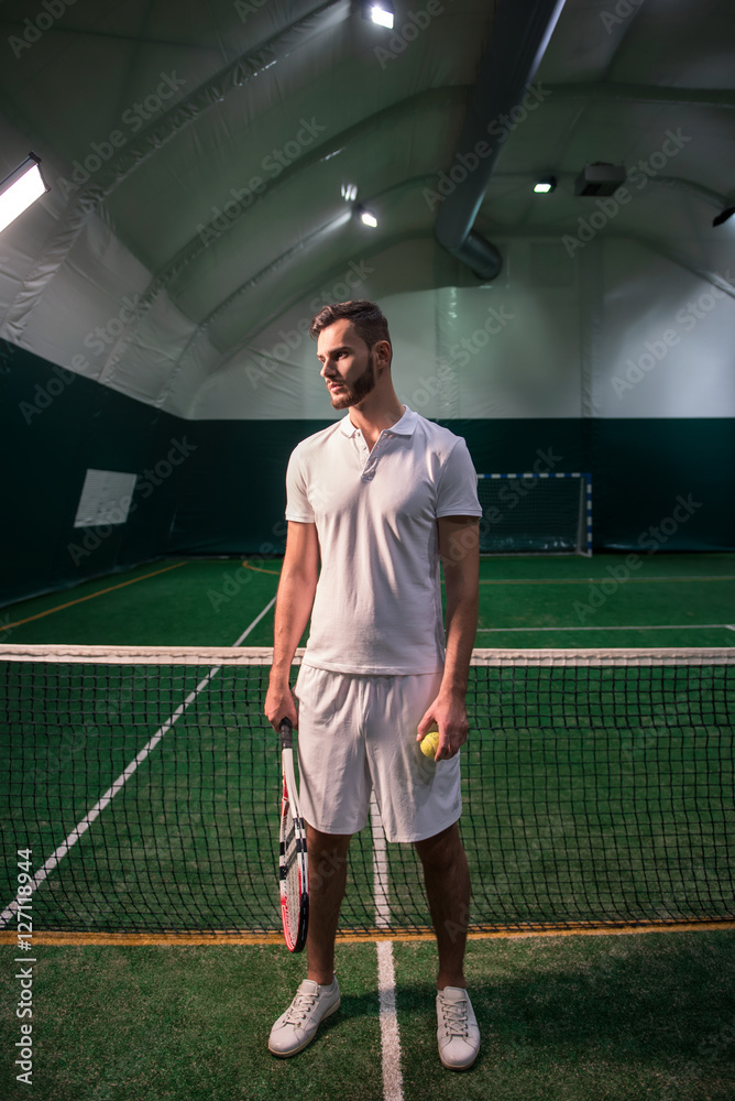 Pleasant confident tennis player standing in the indoor court