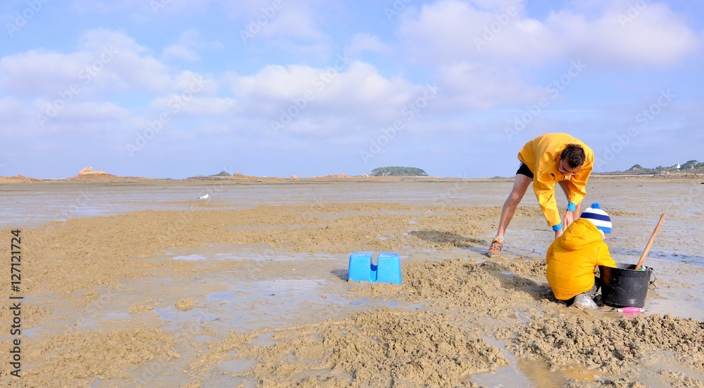 Un père et son fils ramassent des coques dans le sable à marée basse en Bretagne à Buguélès