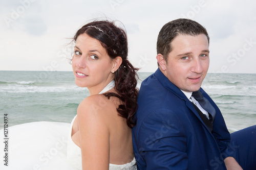 Couple on the beach in wedding dress back to back