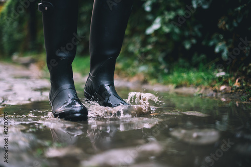 Woman in black rubber boots standing in a puddle with autumn leaves while it's raining. 
