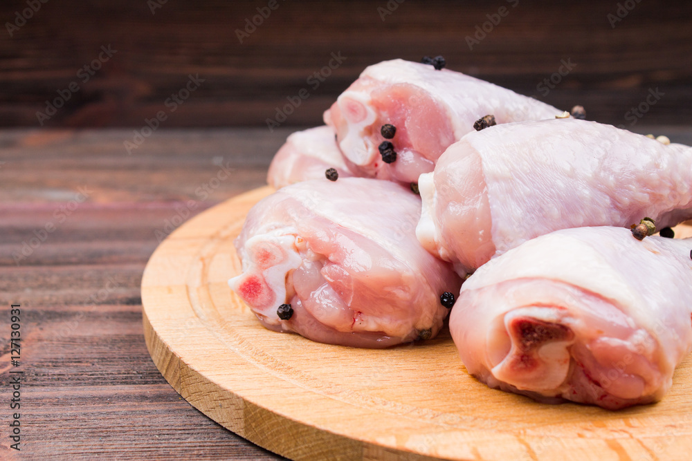 Raw chicken legs with bell pepper on a circular wooden board on