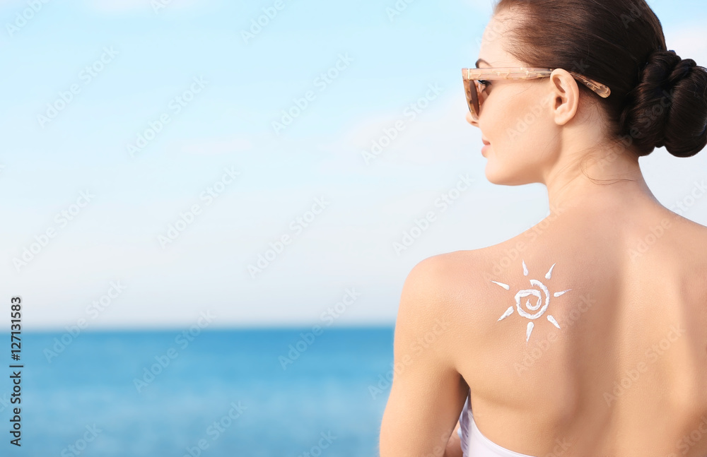 Woman with sun protective lotion in sun shape on shoulder Woman with sun protective lotion in sun shape on shoulder