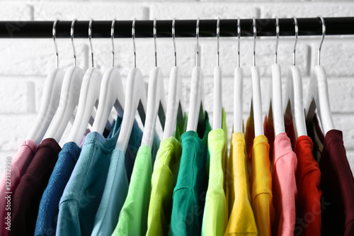 Colorful t-shirts on hangers against light background, close up view