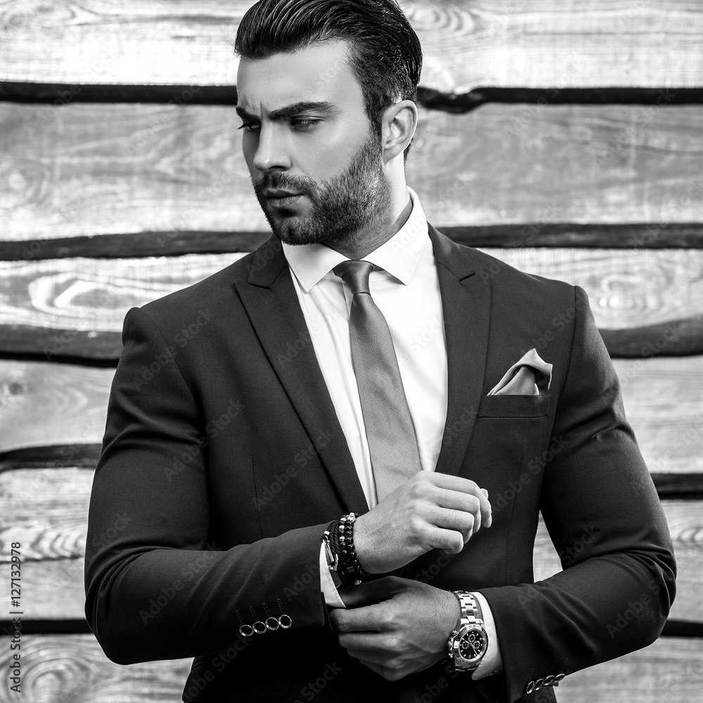 Obraz premium Black-white portrait of beautiful fashionable man in stylish suit against wooden background.