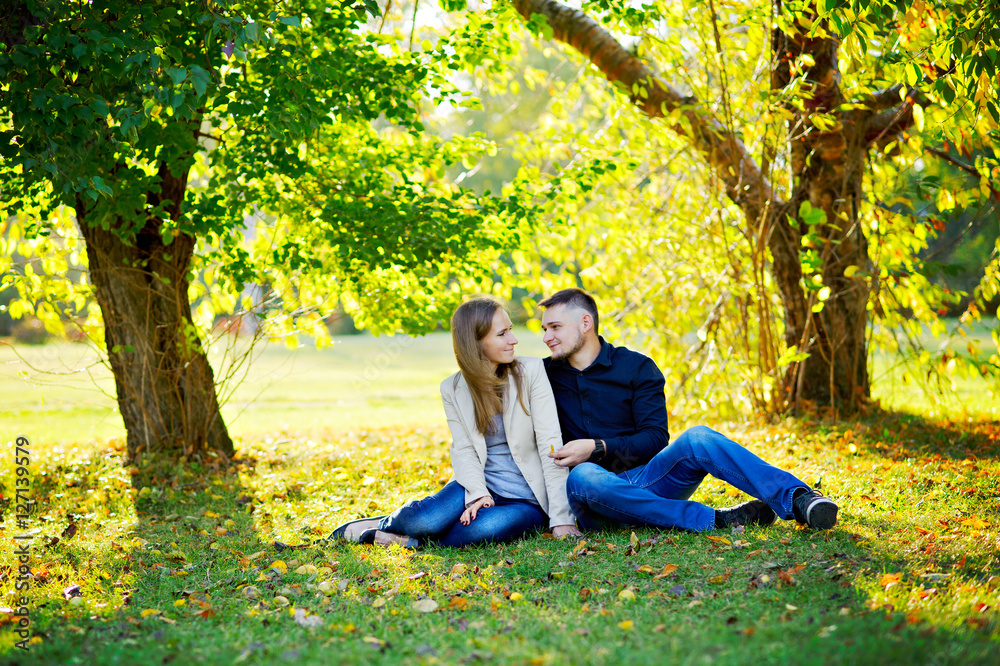 Lovers man and woman sitting in the Park on the grass under a spreading tree, early warm spring, near the fallen yellow leaves, full growth.